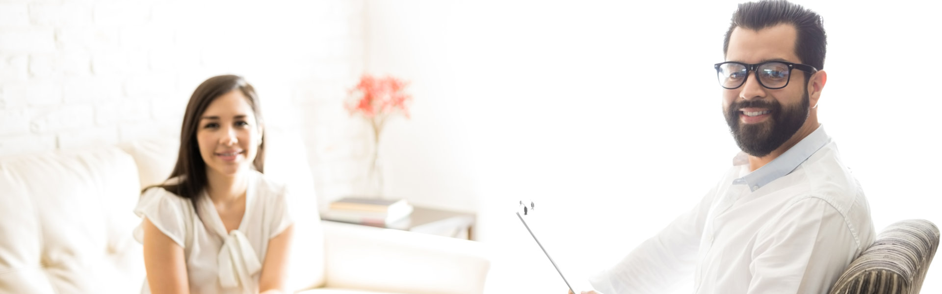 Professional male psychologist with female client sitting on sofa in his office