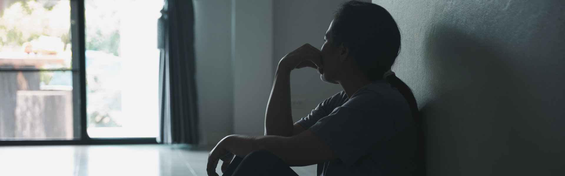 Depressed woman sitting against wall at home with a shadow on wall feeling miserable